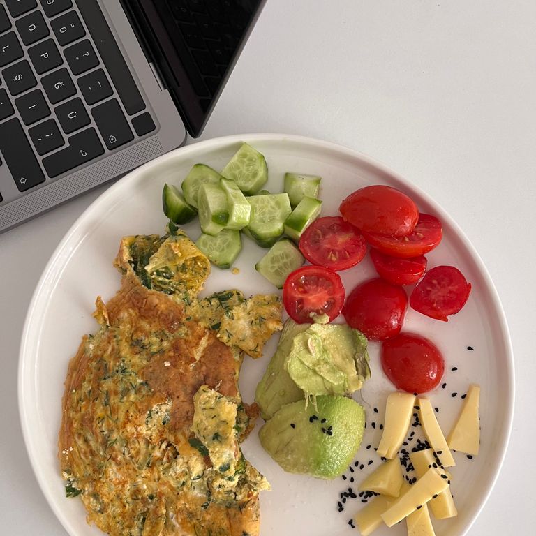 Delicious breakfast plate with omelette, veggies, avocado, and cheese next to a laptop.