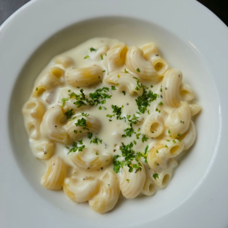 Delicious creamy macaroni pasta served in a white bowl, garnished with fresh herbs.