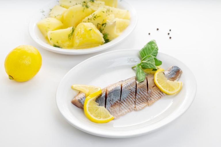 Delicious fish fillet with lemon slices and herb potatoes on white plates.