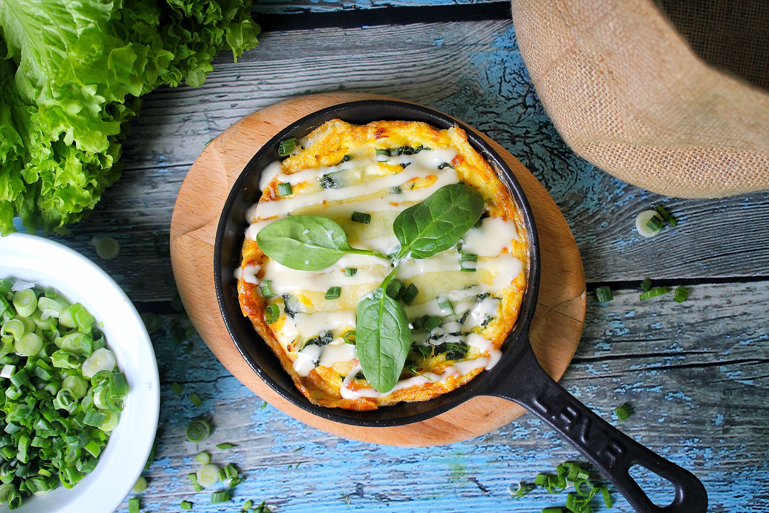 Delicious gourmet omelette with melted cheese and green onions in a skillet, garnished with fresh lettuce.