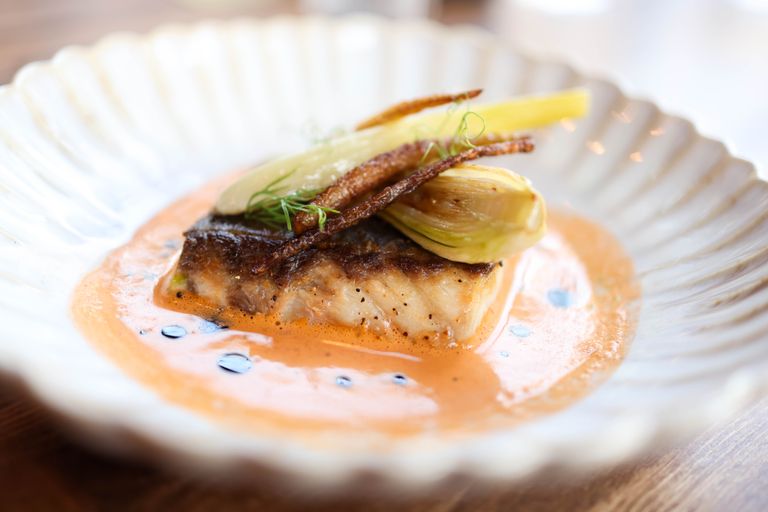Delicious gourmet roasted fish served with vegetables in a creamy sauce on a decorative plate.