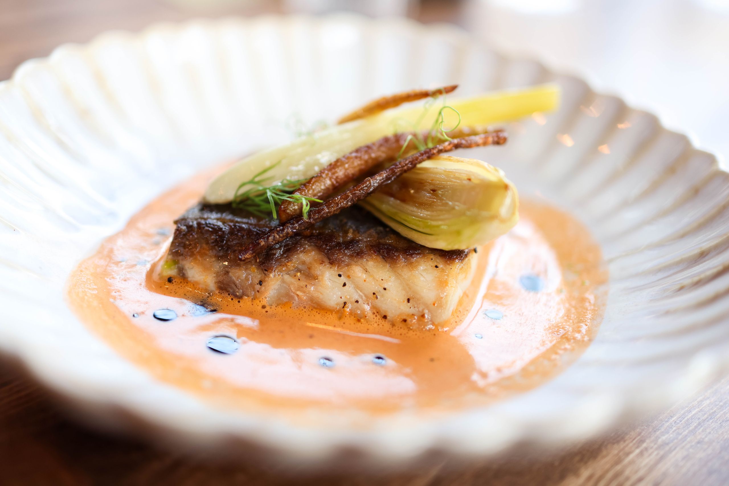 Delicious gourmet roasted fish served with vegetables in a creamy sauce on a decorative plate.