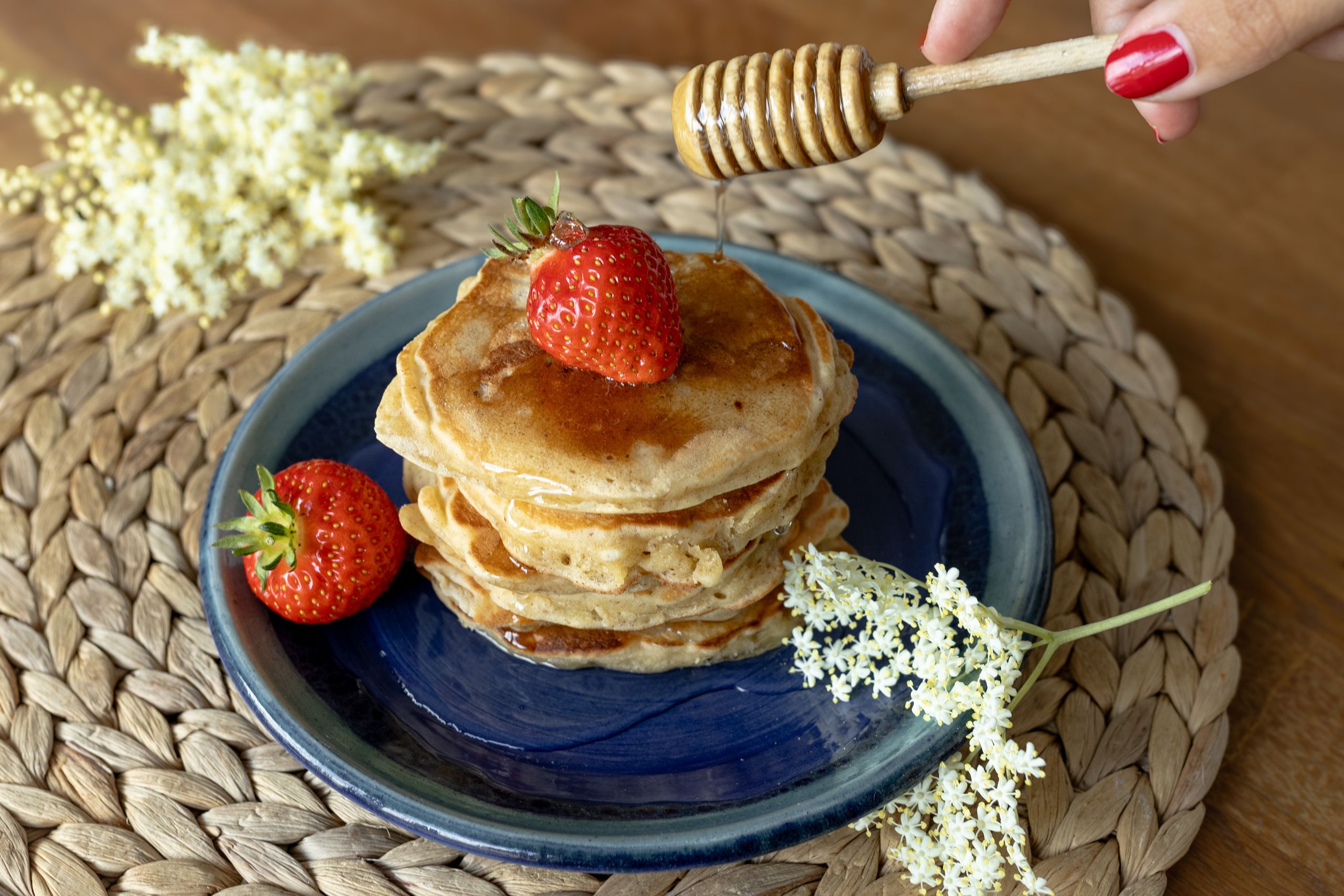 Delicious pancakes topped with fresh strawberries and honey drizzle, garnished with elderflowers.