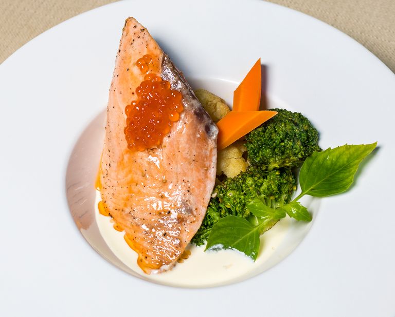 Delicious salmon fillet topped with caviar served with fresh vegetables on a white plate.