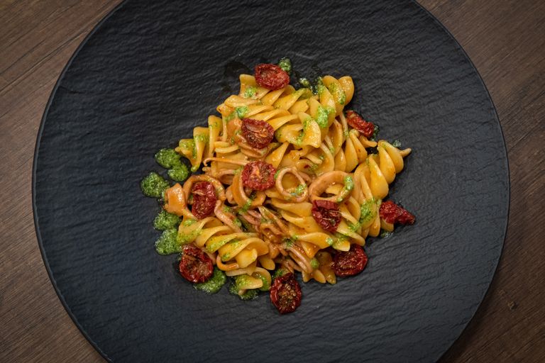 Delicious spiral pasta with roasted cherry tomatoes and pesto sauce on a rustic black plate.
