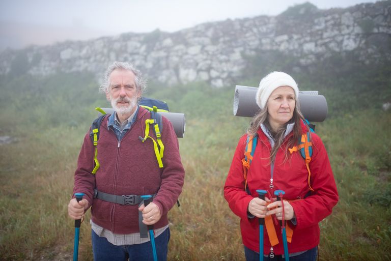 Vitaal ouder wordend echtpaar wandelt met wandelstokken en rugzakken in de natuur