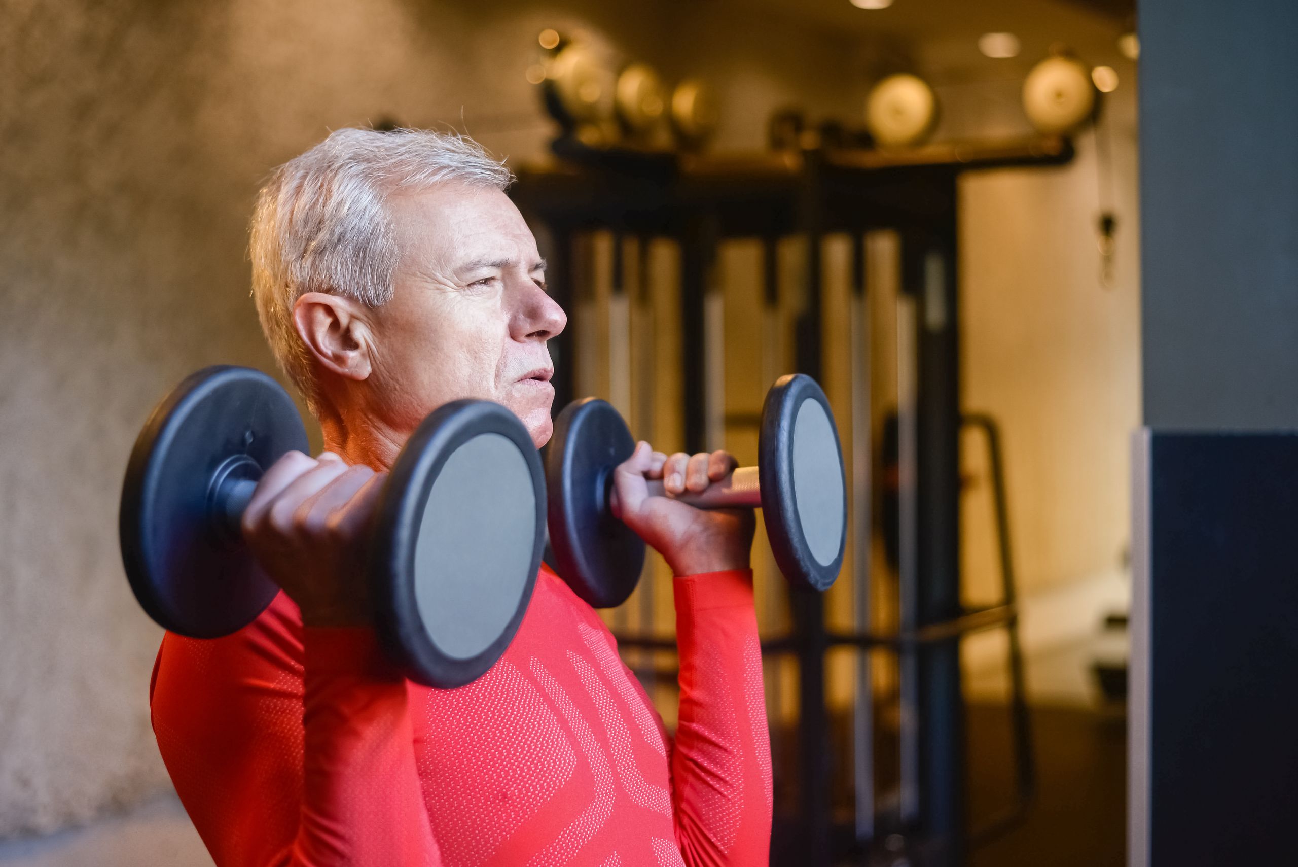 Elderly man lifting dumbbells at the gym to maintain a healthy lifestyle and stay fit.