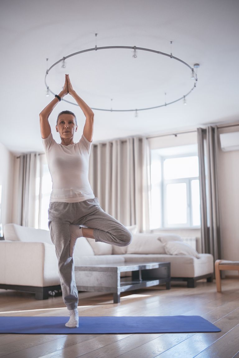 Oudere vrouw doet een balansoefening in tree pose in haar woonkamer