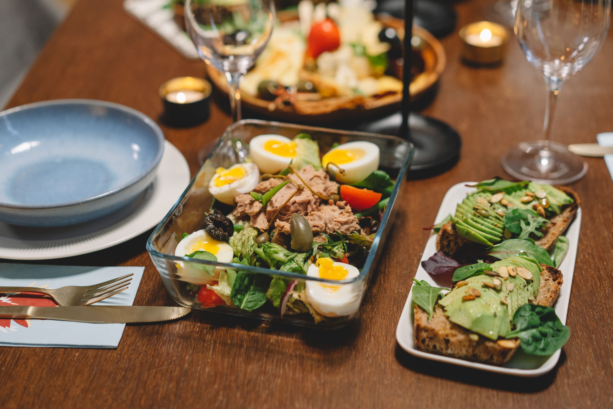 Elegant dining setup with fresh salad, avocado toast, and wine glasses on a wooden table.