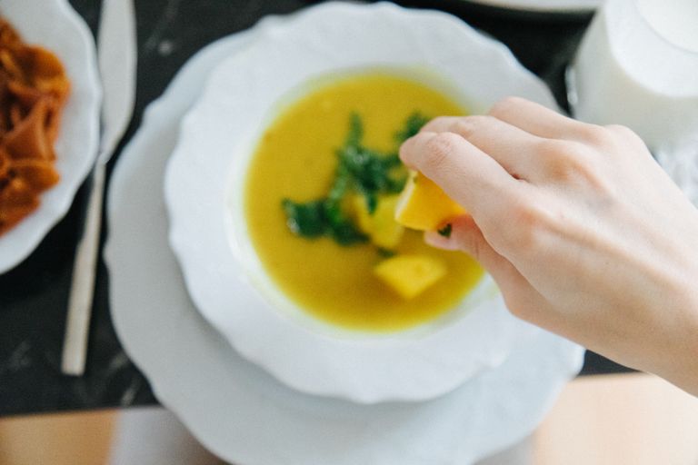 Hand squeezing lemon over lentil soup, enhancing flavor in traditional Turkish setting.