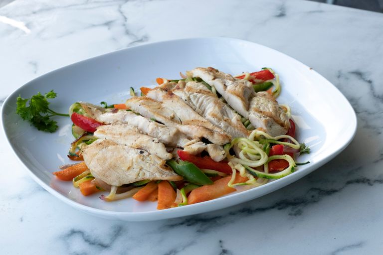 Healthy grilled chicken breast served on zucchini noodles and fresh vegetables.