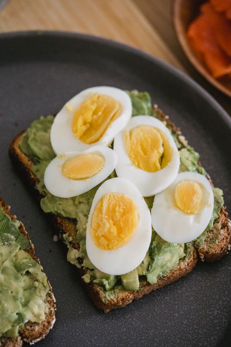 High-angle view of avocado toast topped with boiled eggs, served on a dark plate.