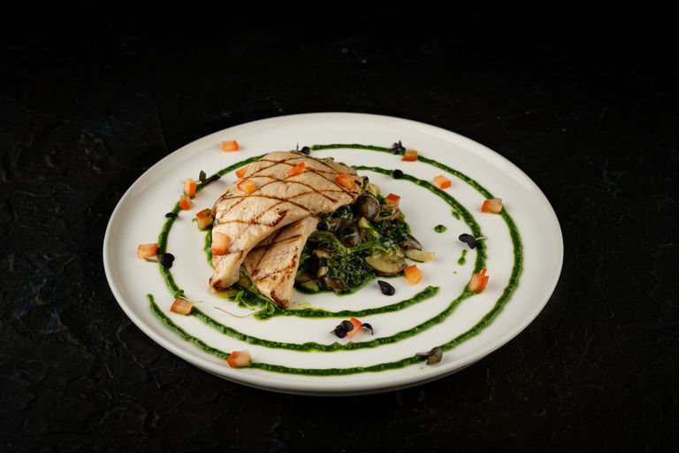 Plate of grilled chicken with greens and vegetables, artfully presented.