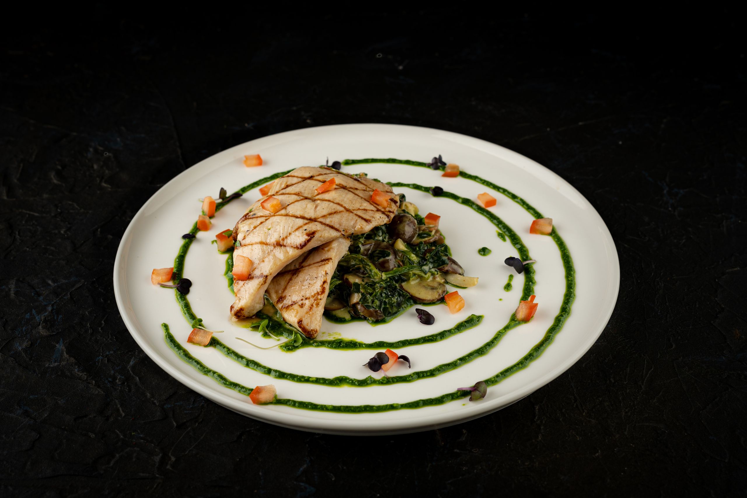 Plate of grilled chicken with greens and vegetables, artfully presented.