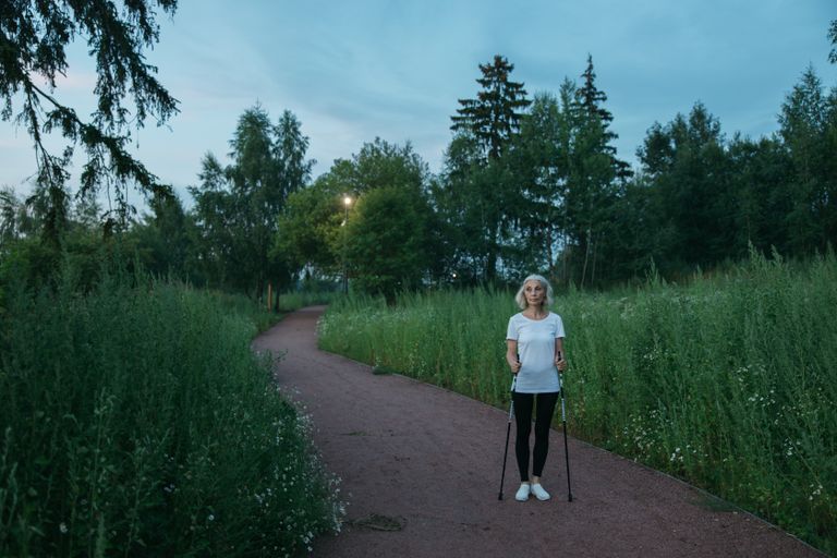 Senior woman exercising with Nordic walking poles in a peaceful green park during daytime.