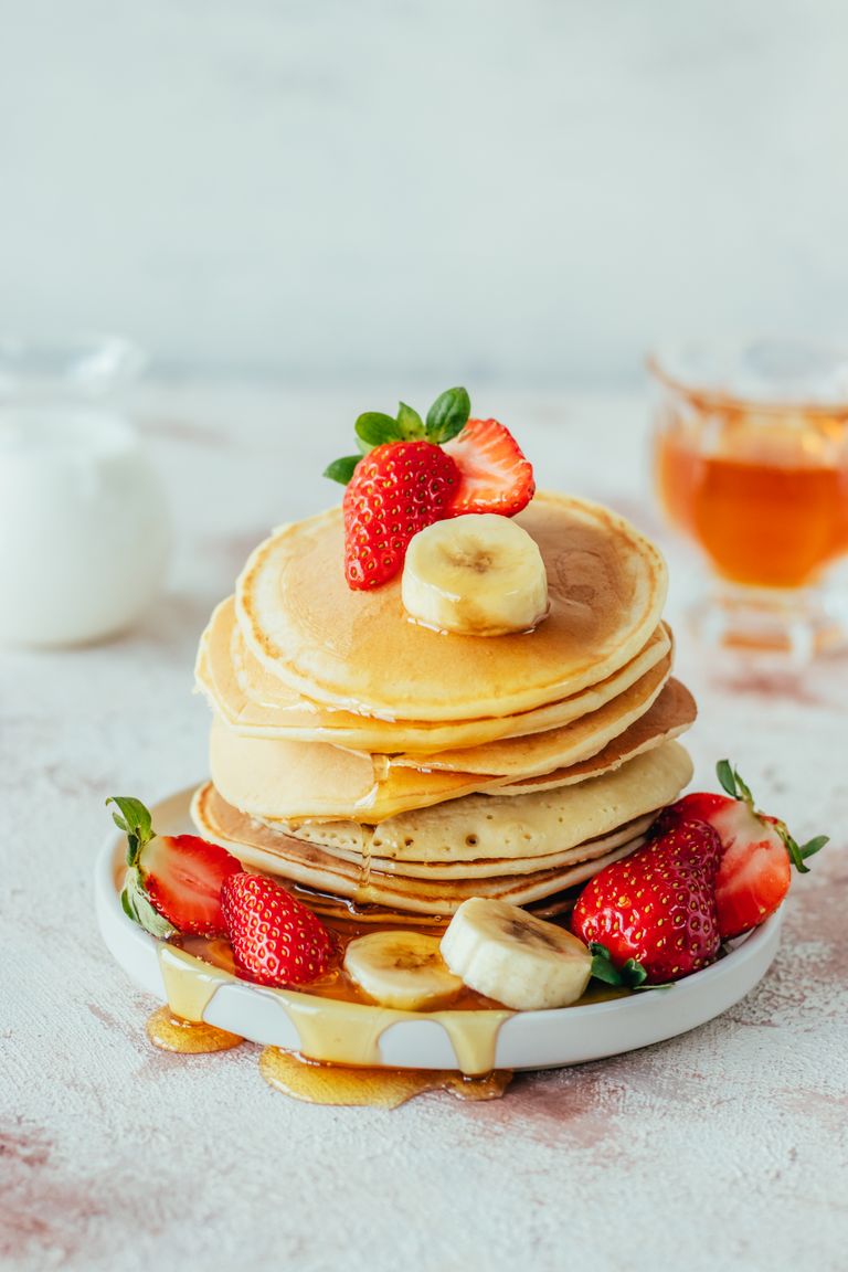 Stack of fluffy pancakes with strawberries, banana, and syrup.