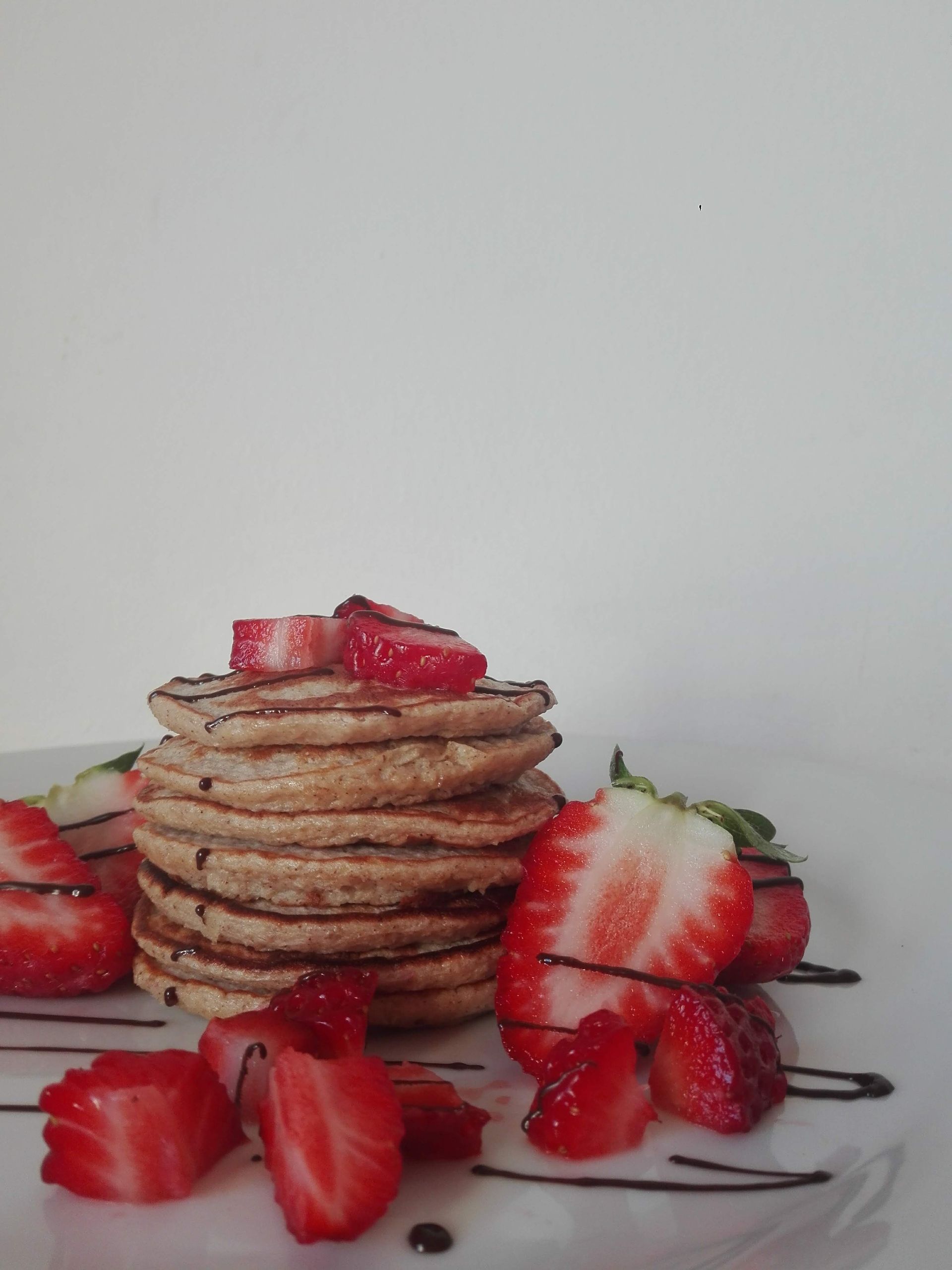 Stack of pancakes topped with fresh strawberries and chocolate syrup on a white plate.