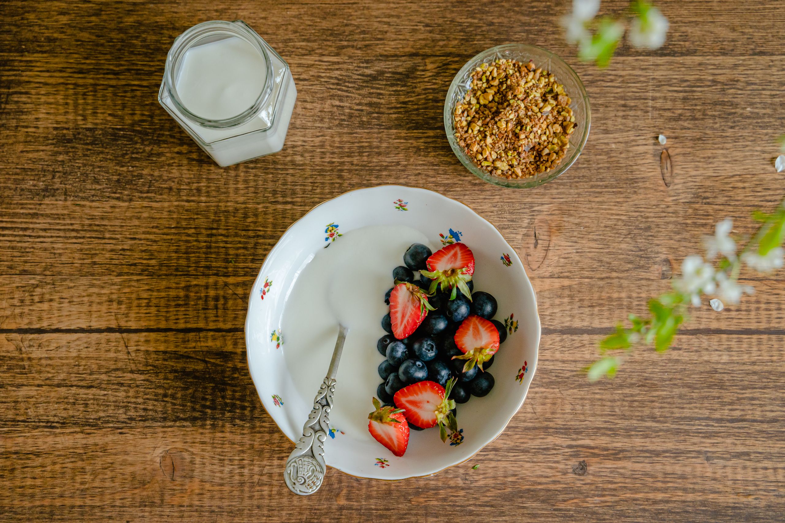 Top view of a bowl of yogurt with fresh strawberries, blueberries, and granola on a wooden table.