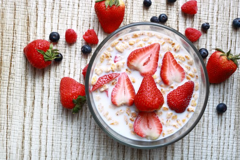 Top view of a cereal bowl with fresh strawberries, blueberries, and milk on a textured surface.