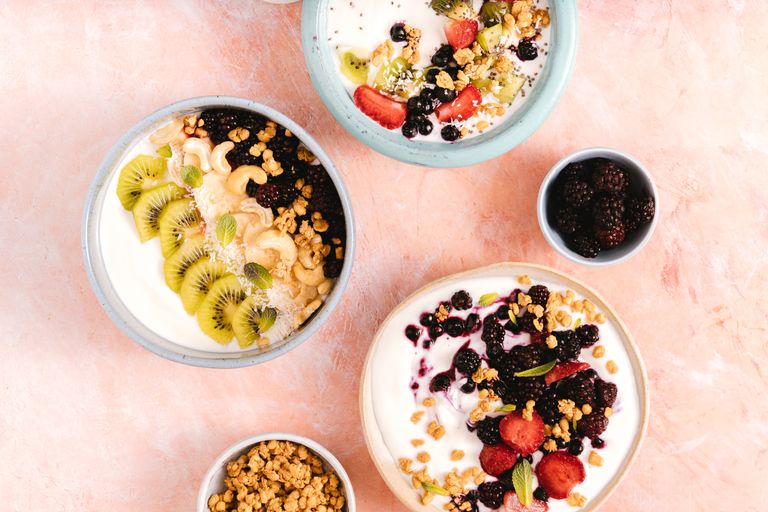 Top view of yogurt bowls topped with fresh fruits and nuts on a textured background.
