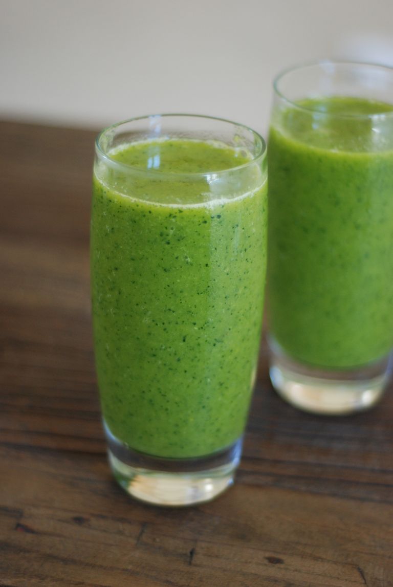 Two green smoothies in glass on a rustic wooden table, embodying freshness and health.