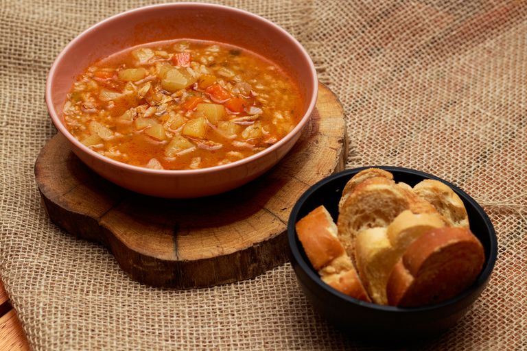 Warm vegetable soup and bread served on rustic surface, perfect for cozy meals.