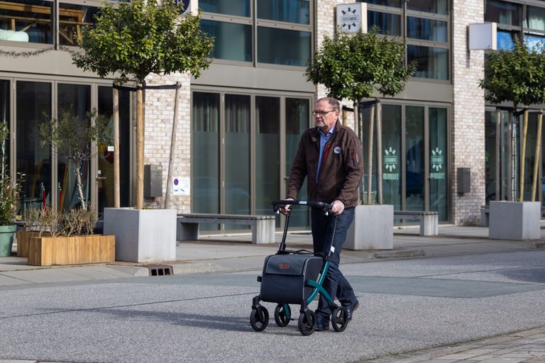 Senior man using a rollator while walking on a city street, showcasing urban mobility.